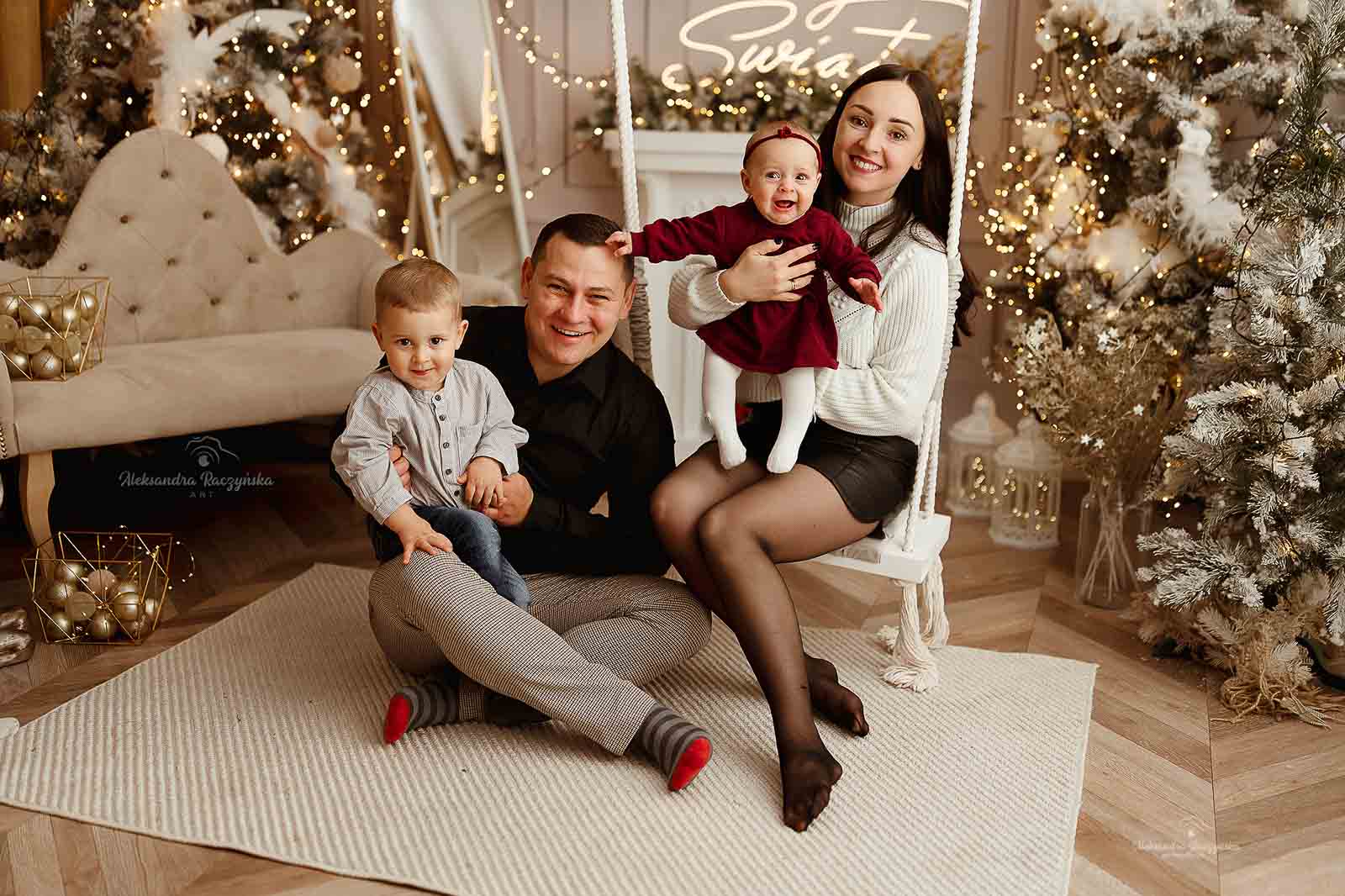 Cała rodzina na huśtawce, w tle choinka i dekoracje w studio Drugi Brzeg w Warszawie – świąteczna sesja fotograficzna w klimacie Bożego Narodzenia.
