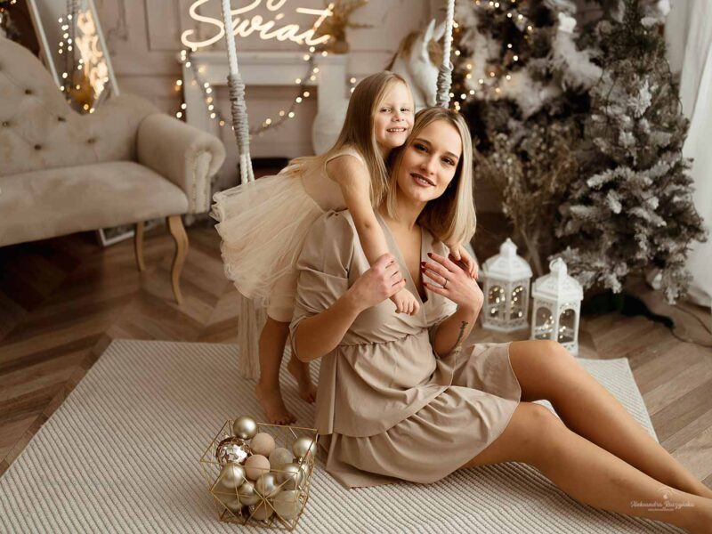 Mama i dziecko przy huśtawce, choinka, bombki w studio Drugi Brzeg w Warszawie – świąteczna sesja fotograficzna w klimacie Bożego Narodzenia.