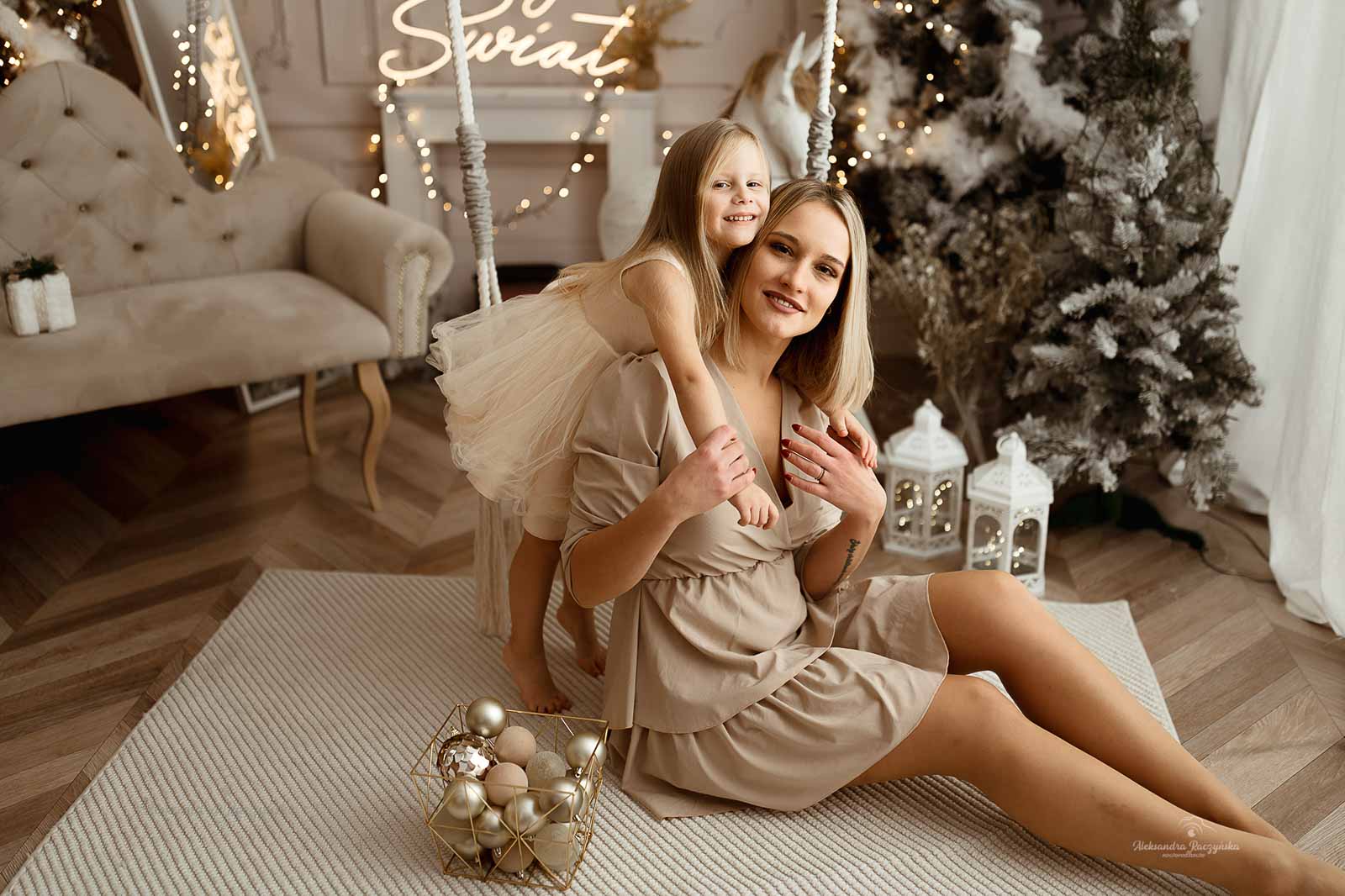 Mama i dziecko przy huśtawce, choinka, bombki w studio Drugi Brzeg w Warszawie – świąteczna sesja fotograficzna w klimacie Bożego Narodzenia.