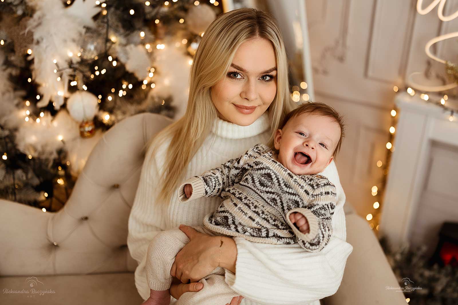 Mama i małe dziecko, biała kanapa i choinka w studio Drugi Brzeg w Warszawie – świąteczna sesja fotograficzna w klimacie Bożego Narodzenia.